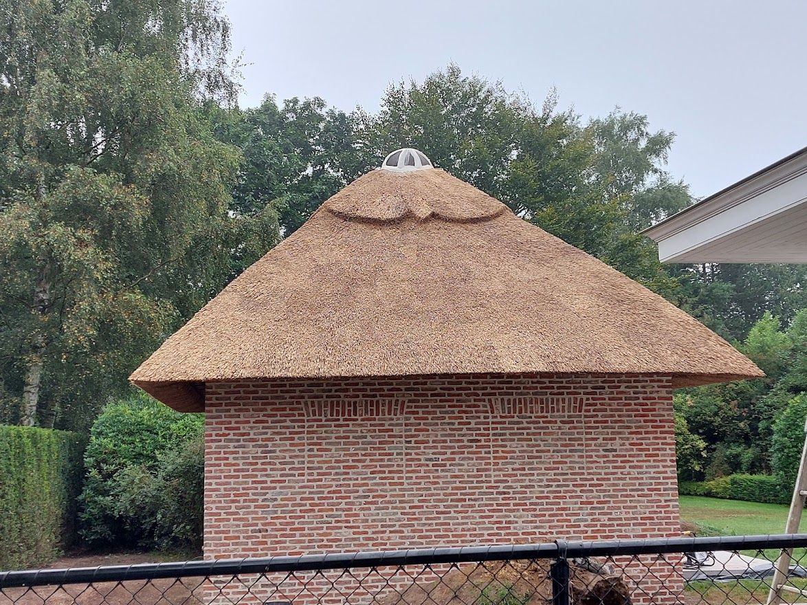 Bijgebouw met puntig rieten dak in een tuin