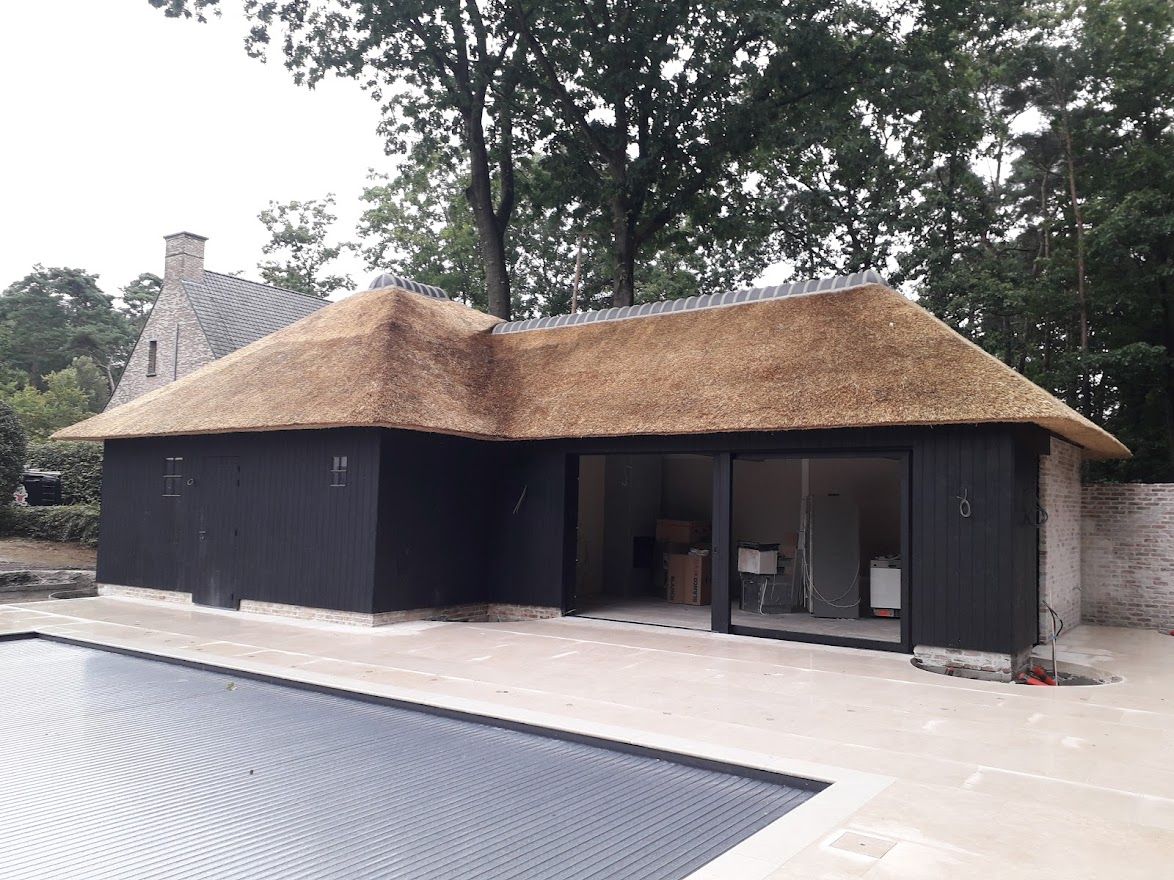 Afgewerkt poolhouse met rieten dak aan een zwembad